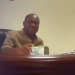 Robert Sarfo-Mensah in the act of taking the cash in his office
